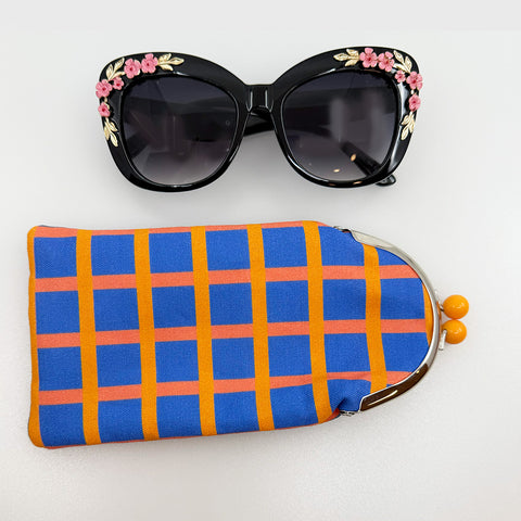 Black sunglasses with floral decorations on a white background, accompanied by a colorful checkered pouch.