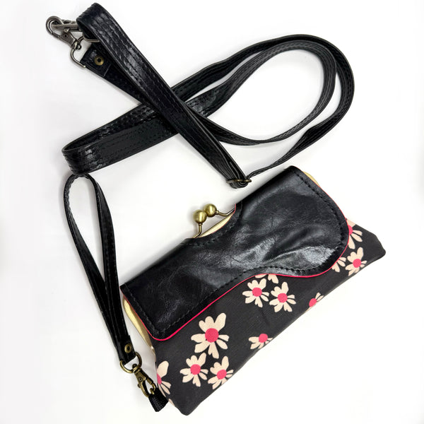 Audrey Wallet Clutch featuring an original print by Jillian Darnell. Featuring cream daisies on a black background with hot pink accents. Two straps are available to use with this item. One is a removable and adjustable cross body strap the second strap is to use the clutch as a wristlet. The folder flap wraps around the antique brass purse frame with twist lock closure and secures with two invisible magnetic snaps. The interior features a small wallet with places to store credit cards and cash. 