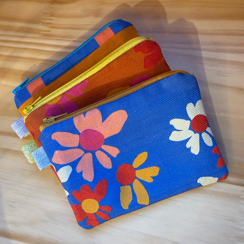Three colorful floral-patterned pouches on a wooden surface