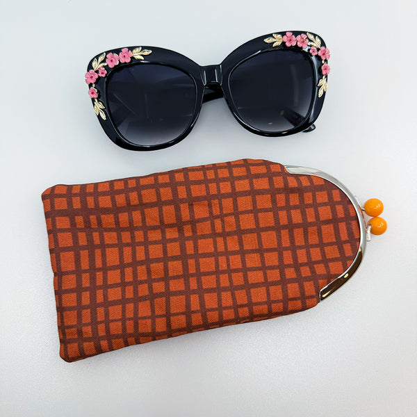 Sunglasses Case in a wavy striped grid pattern in an orange/brown rust color with a twist lock bobble top purse frame in orange. Textile Design by Jillian Darnell.