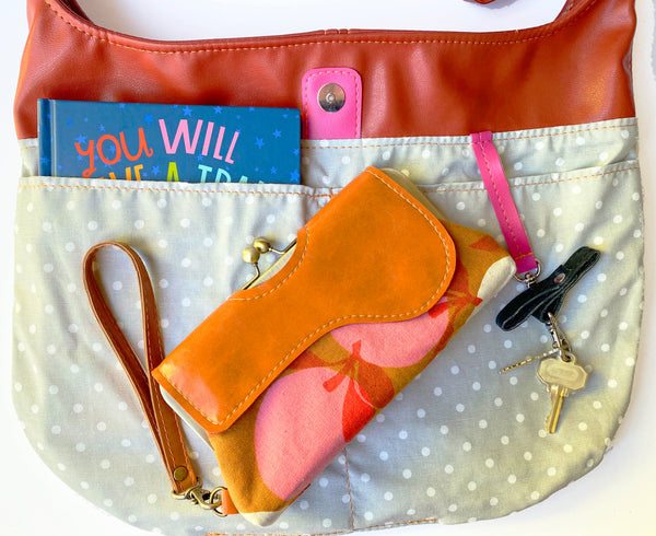 Twyla Tote Lining Photo with grey and white polka dot canvas lining. Showing items that will fit inside the bag, including a book inside of the slip pocket, keys attached to the key snap and a clutch.